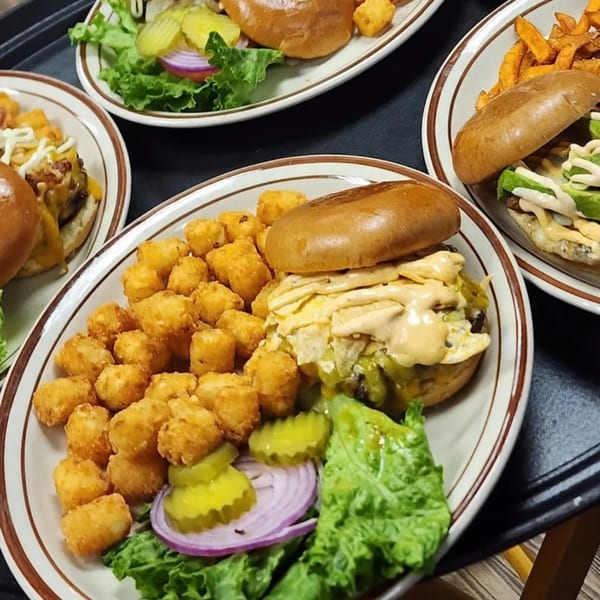 Three Burger Taco burgers with tater tots and sweet potato fries on plates.