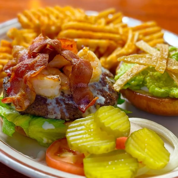A Burger Taco shrimp and bacon burger with waffle fries, guacamole slider, pickles, and tomato.