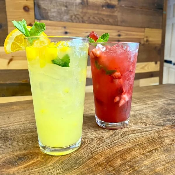 Two refreshing drinks, one yellow with lemon and mint, one red with strawberries and mint.