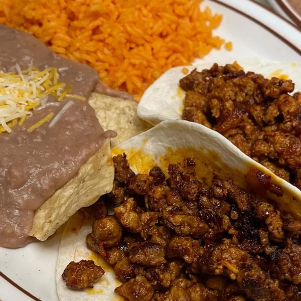 Two Burger Taco tacos with meat, rice, and refried beans with cheese on a white plate.